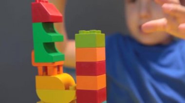 Güzel bir çocuk evde yapı taşlarıyla oynuyor. Şirin, gülümseyen bir çocuk, bir sürü renkli plastik bloğu olan bir lego inşaatçısıyla oynuyor ve bir şehir inşa ediyor. Anaokulu sınıfları.