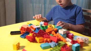 Güzel bir çocuk evde yapı taşlarıyla oynuyor. Şirin, gülümseyen bir çocuk, bir sürü renkli plastik bloğu olan bir lego inşaatçısıyla oynuyor ve bir şehir inşa ediyor. Anaokulu sınıfları.