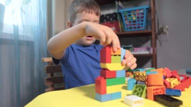 Güzel bir çocuk evde yapı taşlarıyla oynuyor. Şirin, gülümseyen bir çocuk, bir sürü renkli plastik bloğu olan bir lego inşaatçısıyla oynuyor ve bir şehir inşa ediyor. Anaokulu sınıfları.