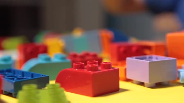 一个漂亮的男孩在家里玩积木游戏 一个可爱的面带微笑的男孩正在和一个带着许多彩色塑料块的法律构造师玩耍 他正在建造一座城市 学前教育课程 — 图库视频影像