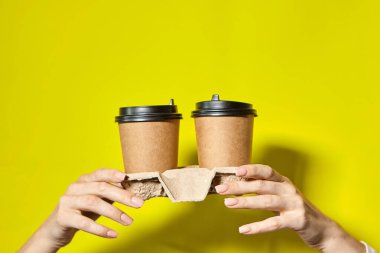 Siyah kapaklı iki bardak kahverengi kağıt tutan eller. İki özel kahve ya da tanıtım. Sarı ekranda iki bardak tutan eller. Çay ya da kahve. Siyah kapaklı kahverengi kağıt bardak..