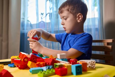 Güzel bir çocuk evde yapı taşlarıyla oynuyor. Şirin, gülümseyen bir çocuk, bir sürü renkli plastik bloğu olan bir lego inşaatçısıyla oynuyor ve bir şehir inşa ediyor. Anaokulu sınıfları.