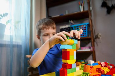 Güzel bir çocuk evde yapı taşlarıyla oynuyor. Şirin, gülümseyen bir çocuk, bir sürü renkli plastik bloğu olan bir lego inşaatçısıyla oynuyor ve bir şehir inşa ediyor. Anaokulu sınıfları.