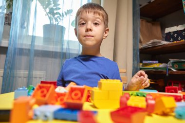 Güzel bir çocuk evde yapı taşlarıyla oynuyor. Şirin, gülümseyen bir çocuk, bir sürü renkli plastik bloğu olan bir lego inşaatçısıyla oynuyor ve bir şehir inşa ediyor. Anaokulu sınıfları.