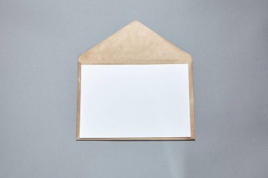 Gri arka planda kahverengi bir zarfın beyaz kağıt maketi. Beyaz kağıt boş, okaliptüs dalı gri masada. Davetiye kartı modeli. Düz konum, üst görünüm, kopyalama alanı, modelleme