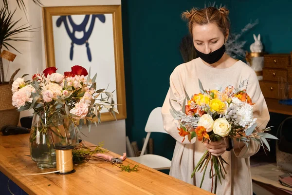 花は色で動作します 花売りは将来の花束に花を選ぶ 花屋に立つ仮面の花屋さんで 花瓶の花をチェックする — ストック写真