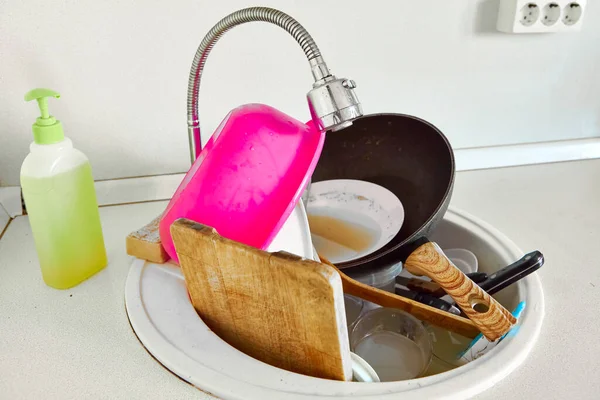There are a lot of dirty dishes in the kitchen sink. Housework, cooking and cleaning.