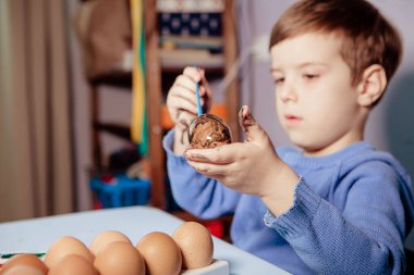 Küçük bir çocuk masaya mavi bir arka plan üzerine paskalya yumurtası çiziyor. Küçük çocuk evde boyalı Paskalya yumurtalarını boyuyor. Çocukların Paskalya yaratıcılığı. Paskalya yumurtalarını bir çocuk süslüyor..