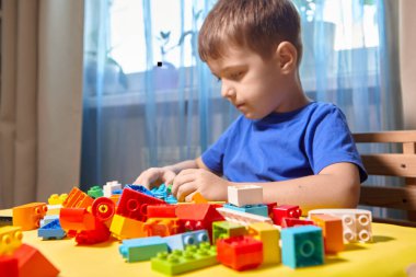 Güzel bir çocuk evde yapı taşlarıyla oynuyor. Şirin, gülümseyen bir çocuk, bir sürü renkli plastik bloğu olan bir lego inşaatçısıyla oynuyor ve bir şehir inşa ediyor. Anaokulu sınıfları.