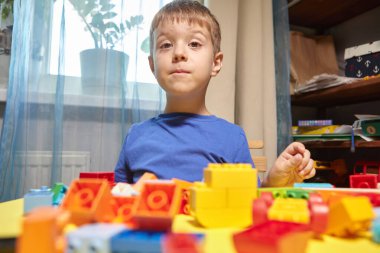Güzel bir çocuk evde yapı taşlarıyla oynuyor. Şirin, gülümseyen bir çocuk, bir sürü renkli plastik bloğu olan bir inşaatçıyla oynuyor ve bir şehir inşa ediyor. Anaokulu sınıfları.