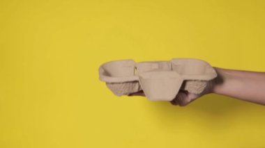 Sarı arka planda yakın plan, kadınların elleri bir stantta kahve ile iki kağıt bardak tutuyor. Seninle kahve ya da çay. Bir fiyatına iki terfi, sarı arka planda kahve teslimatı.