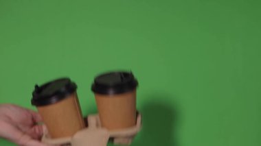 Yeşil arka planda yakın plan, bir kadının eli ayakta kahve olan bir kağıt bardağı tutuyor. Kahve ya da çay. İnsanlar birbirlerine kahve ve kahve dağıtırlar..
