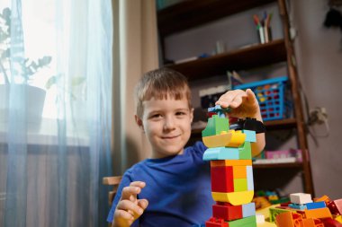 Güzel bir çocuk evde yapı taşlarıyla oynuyor. Şirin, gülümseyen bir çocuk, bir sürü renkli plastik bloğu olan bir inşaatçıyla oynuyor ve bir şehir inşa ediyor. Anaokulu sınıfları.