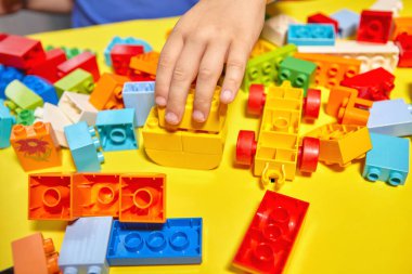 Güzel bir çocuk evde yapı taşlarıyla oynuyor. Şirin, gülümseyen bir çocuk, bir sürü renkli plastik bloğu olan bir inşaatçıyla oynuyor ve bir şehir inşa ediyor. Anaokulu sınıfları.