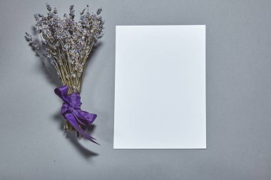 Beyaz kağıt kaplamalı lavanta çiçekleri gri arka planda. Beyaz kağıt boş, gri masada kurumuş çiçekler. Davetiye kartı mockup.Düz konum, üst görünüm, kopyalama alanı, maket