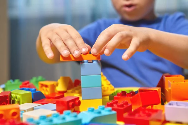 Güzel bir çocuk evde yapı taşlarıyla oynuyor. Şirin, gülümseyen bir çocuk, bir sürü renkli plastik bloğu olan bir inşaatçıyla oynuyor ve bir şehir inşa ediyor. Anaokulu sınıfları.
