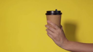 Sarı arka planda yakın plan, bir kadının eli ayakta kahve olan bir kağıt bardağı tutar. Kahve ya da çay. İnsanlar birbirlerine kahve ve kahve dağıtırlar..