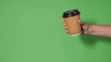 Yeşil arka planda yakın plan, bir kadının eli ayakta kahve olan bir kağıt bardağı tutuyor. Kahve ya da çay. İnsanlar birbirlerine kahve ve kahve dağıtırlar..