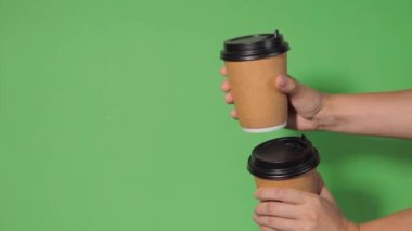 Yeşil arka planda yakın plan, bir kadının eli ayakta kahve olan bir kağıt bardağı tutuyor. Kahve ya da çay. İnsanlar birbirlerine kahve ve kahve dağıtırlar..
