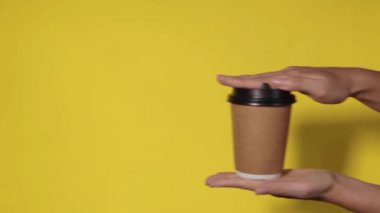 Sarı arka planda yakın plan, bir kadının eli ayakta kahve olan bir kağıt bardağı tutar. Kahve ya da çay. İnsanlar birbirlerine kahve ve kahve dağıtırlar..