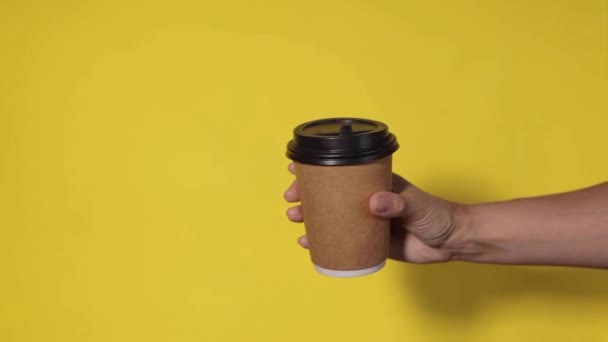 黄色の背景にクローズアップし 女性の手はスタンドでコーヒーと紙コップを保持しています コーヒーや紅茶を移動します コーヒーをもう一杯渡しコーヒーを配達し — ストック動画