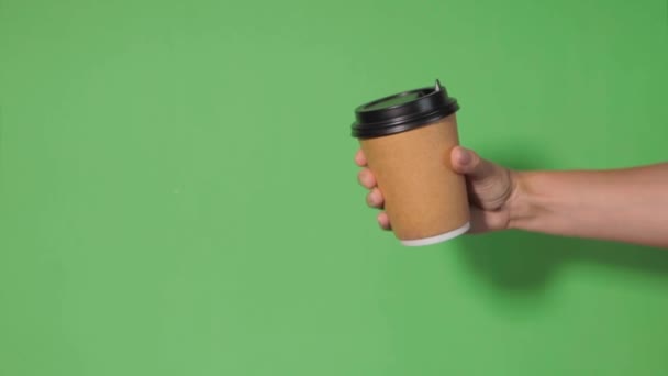 在绿色背景的特写下 一个女人的手拿着一个纸杯 咖啡放在架子上 咖啡或茶去 人们相互递给对方一杯咖啡 送咖啡 — 图库视频影像
