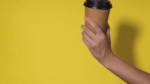 黄色の背景にクローズアップし 女性の手はスタンドでコーヒーと紙コップを保持しています コーヒーや紅茶を移動します コーヒーをもう一杯渡しコーヒーを配達し — ストック動画