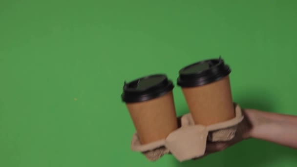 緑を背景に 女性の手はスタンドでコーヒーと紙コップを保持しています コーヒーや紅茶を移動します コーヒーをもう一杯渡しコーヒーを配達し — ストック動画