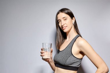 Spor elbiseli ve kablosuz kulaklıklı bir kadın su içiyor. Sağlıklı yaşam tarzı ve spor aktiviteleri kavramı