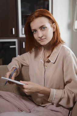 Oturma odasındaki kanepede oturan, kızıl saçlı, beyaz, güzel bir kadın elinde bir defter tutuyor. Kameraya bakıyor, gülümsüyor ve gülüyor. Neşe, sıcaklık, mutluluk..