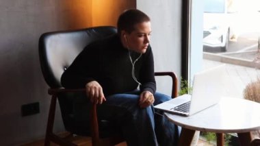 Eğitim ve uzaktan çalışma kavramı. Gözlüklü, kısa saçlı ve burun piercingli genç bir kadın bir kafede oturuyor ve bir dizüstü bilgisayar üzerinde çalışıyor. Serbest çalışma ve uzak çalışma veya eğitim kavramı.