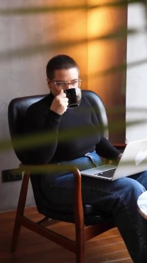 Eğitim ve uzaktan çalışma kavramı. Gözlüklü, kısa saçlı ve burun piercingli genç bir kadın bir kafede oturuyor ve bir dizüstü bilgisayar üzerinde çalışıyor. Serbest çalışma ve uzak çalışma veya eğitim kavramı.