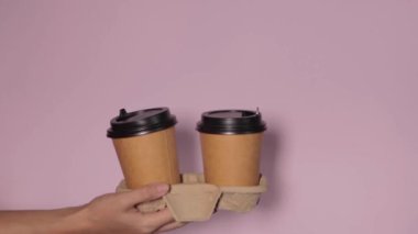Renkli arka planda bardakları tutan eller. Çay ya da kahve. Siyah kapaklı kahverengi kağıt bardak..