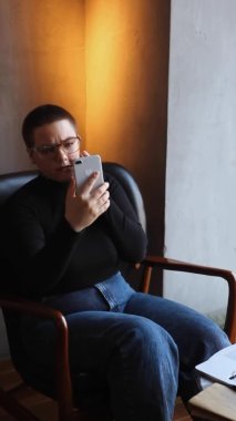 Eğitim ve uzaktan çalışma kavramı. Gözlüklü, kısa saçlı ve burun piercingli genç bir kadın bir kafede oturuyor ve bir dizüstü bilgisayar üzerinde çalışıyor. Serbest çalışma ve uzak çalışma veya eğitim kavramı.