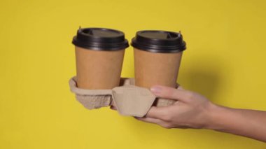 Renkli arka planda bardakları tutan eller. Çay ya da kahve. Siyah kapaklı kahverengi kağıt bardak..