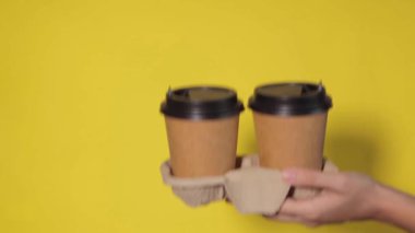 Renkli arka planda bardakları tutan eller. Çay ya da kahve. Siyah kapaklı kahverengi kağıt bardak..