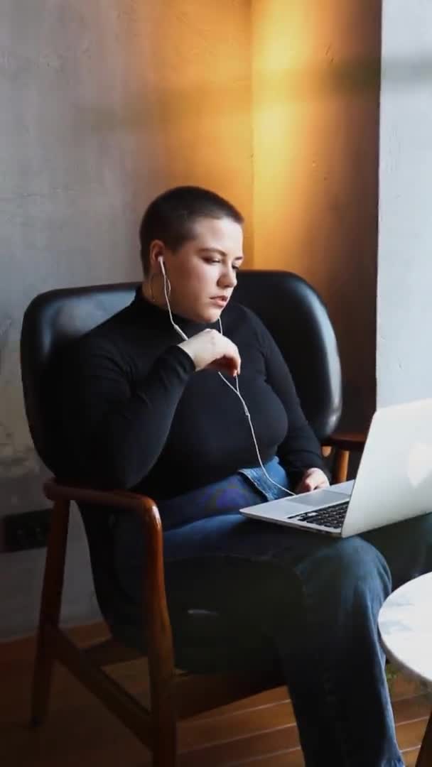 教育と遠隔作業の概念 ショートヘア 鼻ピアスをした若い女性がカフェに座ってノートパソコンで作業しています フリーランスとリモートワークやトレーニングの概念 — ストック動画