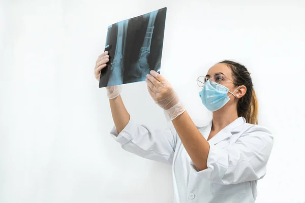 Young doctor with a mask examining a leg X-ray on a white background