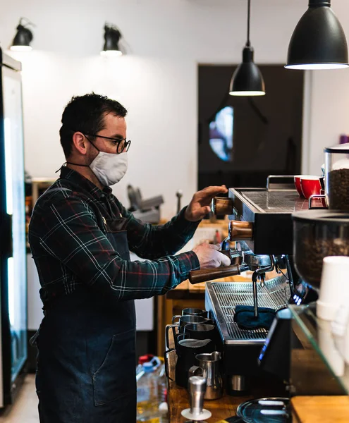 Caucasian barista with mask making coffee in a coffee shop