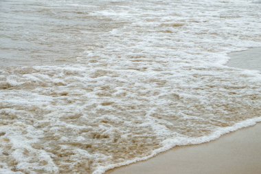 Denizin kıyısında dalgalar kırılıyor. Islak kumda deniz köpüğüne yakın çekim.