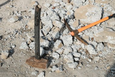 Geological pick with orange handle on the stones next to old hammer.