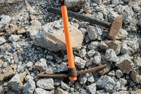 Geological pick with orange handle on the stones next to old hammer.