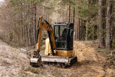 Çam ormanında sarı kuşak kazıcı. Hidrolik toprak taşıyıcı hasatçı. Dönüşümlü operatör taksisi. İnşaat endüstrisi.