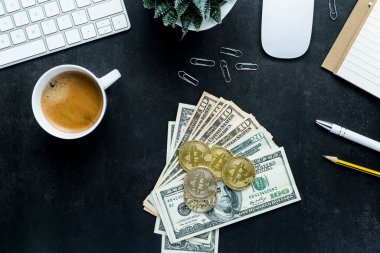 Düz görünüm ofis masası klavye ve akıllı telefon, saat, bitki, kahve, Amerikan dolarları ve siyah arka planda bitcoin ile çalışma alanı