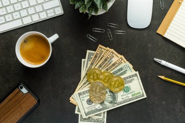 Düz görünüm ofis masası klavye ve akıllı telefon, saat, bitki, kahve, Amerikan dolarları ve siyah arka planda bitcoin ile çalışma alanı