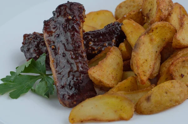 Appetizing, baked pork ribs and baked potatoes on a white plate.