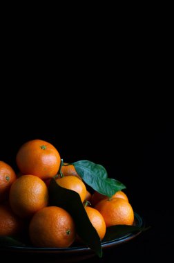 Siyah bir zeminde, yazı yazmak için alanı olan bir tabakta mandalinaların hayatı.
