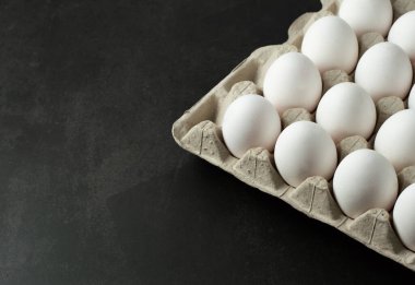 Siyah masa üzerinde beyaz yumurtalı bir kağıt yumurta tepsisi var. Arka planda mesaj yazmak için yer var..