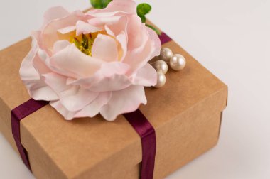 Hediye kutusu yapay şakayıkla süslenir. Beyaz arka planda yeşillik vardır..