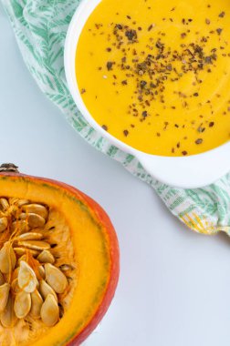 Beyaz arka planda, beyaz tabakta kesilmiş bir balkabağı ve balkabağı çorbasının bulanık görüntüsü..